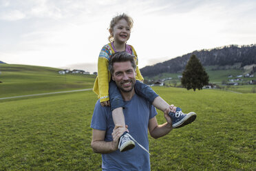 Austria, Tyrol, Walchsee, happy father carrying daughter piggyback on an alpine meadow - JLOF00219