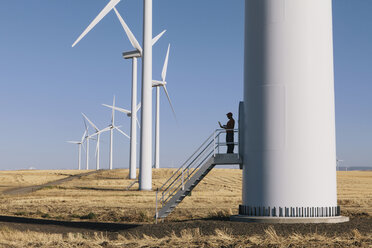 Ein Windparktechniker steht mit einem Laptop am Fuß einer Turbine in einem Windpark in der freien Natur bei Palouse. - MINF05889