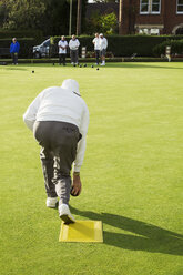 Ein Rasenbowlingspieler steht auf einer kleinen gelben Matte und bereitet sich darauf vor, eine Kugel auf das Grün, die glatte Rasenfläche, zu werfen. - MINF05895