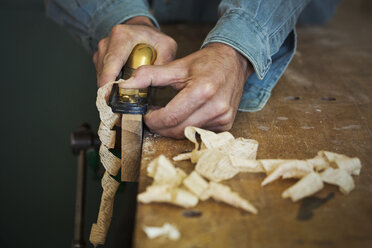 Ein Handwerker hält einen Speichenfräser in der Hand und formt damit ein Stück Holz in einer Klemme. - MINF05903