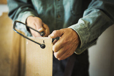 Ein Mann arbeitet mit einer Handsäge an einem Stück Holz. - MINF05905