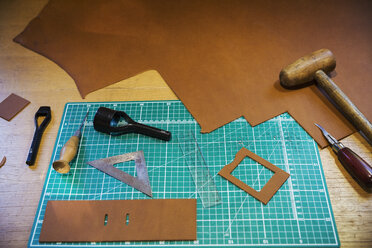 Werkbank und Schneidematte mit einem großen glatten Stück braunen Leders und Werkzeugen zum Abmessen, Schneiden und Nähen, Lederbearbeitungswerkzeuge. - MINF05910