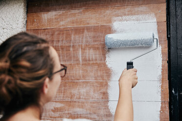 Eine Frau malt mit einer Farbrolle Holzbretter an eine Wand. - MINF05914