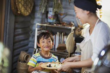 Eine lächelnde Frau und ein Junge stehen in einer Küche und halten einen Teller mit Essen. - MINF05931