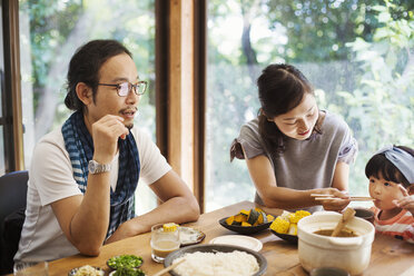 Ein Mann, eine Frau und ein junges Mädchen sitzen an einem Tisch mit Schüsseln voller Essen und essen gemeinsam. - MINF05936