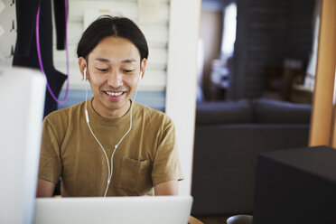 Smiling man sitting indoors at desk, wearing headphones. - MINF05940