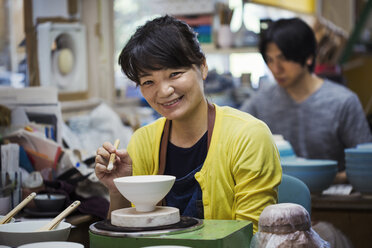 Smiling woman and man sitting in a workshop, working on Japanese porcelain bowls. - MINF05962