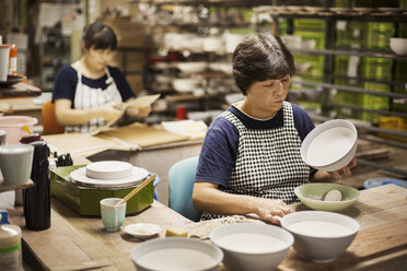 Two women sitting in a workshop, working on Japanese porcelain bowls. - MINF05967