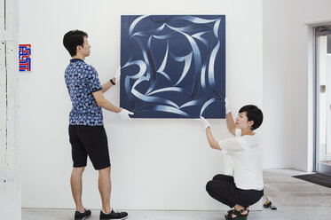 Mann in blauem Hemd und Frau in weißem Hemd hängen modernes Gemälde an weißer Wand in Kunstgalerie. - MINF05971