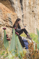 Spanien, Alquezar, junge Frau, die auf einem Felsen sitzt und ein Smartphone benutzt - AFVF01307