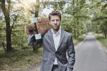 Portrait of businessman carrying skateboard on rural road - RORF01362