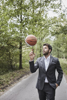 Geschäftsmann balanciert Basketball auf Landstraße - RORF01364