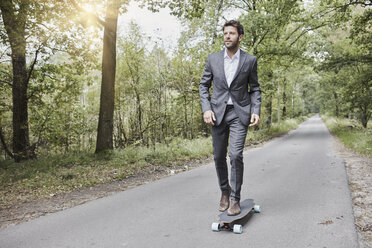 Businessman riding skateboard on rural road - RORF01367