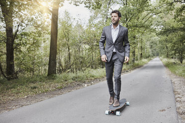 Geschäftsmann fährt Skateboard auf Landstraße - RORF01367