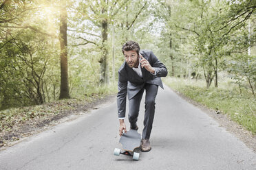 Geschäftsmann zu Fuß mit Skateboard und Smartphone auf Landstraße - RORF01374