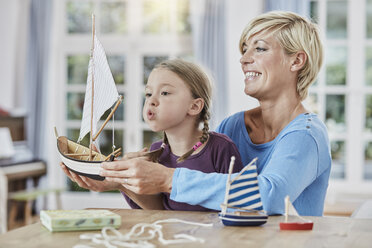 Happy mother and daughter playing with model boat at home - RORF01395