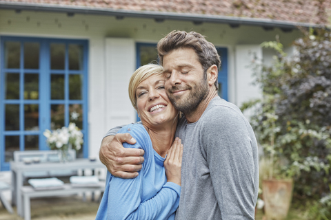 Glückliches Paar, das sich vor seinem Haus umarmt, lizenzfreies Stockfoto