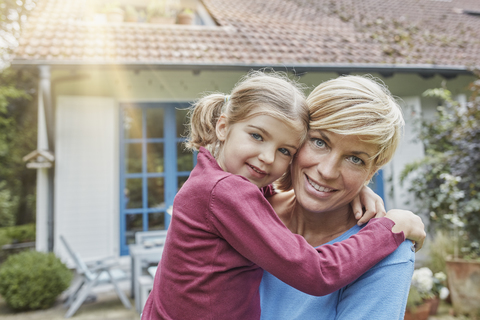 Portrait of smiling mother carrying daughter in front of their home stock photo