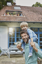 Portrait of happy father carrying son on shoulders in front of their home - RORF01430