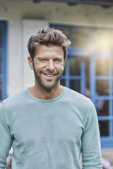 Portrait of smiling man in front of house with blue window - RORF01431