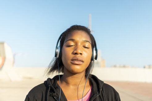 Junge sportliche Frau hört Musik mit Kopfhörern, Augen geschlossen - AFVF01344