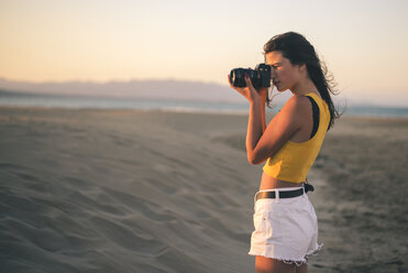 Teenage girl taking photos with camera on the beach at sunset - ACPF00154