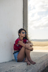 Porträt eines Mädchens mit Sonnenbrille, das unter den Sonnenschirmen sitzt und in die Ferne schaut - ACPF00159