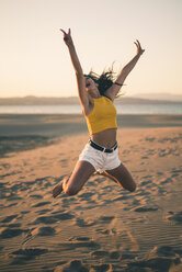 Happy teenage girl jumping in the air on the beach at sunset - ACPF00183