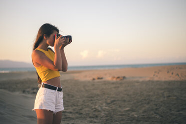 Teenage girl taking photos with camera on the beach at sunset - ACPF00185