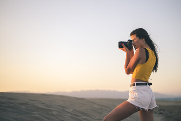 Teenage girl taking photos with camera on the beach at sunset - ACPF00186