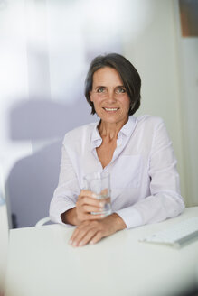 Porträt einer reifen Geschäftsfrau mit einem Glas Wasser, die am Schreibtisch sitzt - PNEF00844