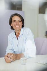 Porträt einer lächelnden reifen Geschäftsfrau, die am Schreibtisch sitzt - PNEF00846