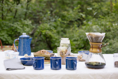 Tisch in einem Garten, mit Kaffeemaschine, Tassen und Schüsseln, Kuchen und Müsli. - MINF06007