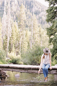 Frau sitzt auf einer Holzbrücke über einen Bach. - MINF06034