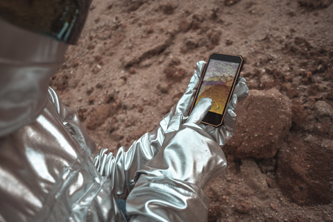 Spaceman examining new planet, using smartphone stock photo