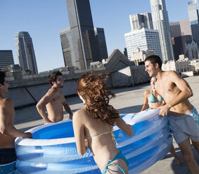 A group of men and women carrying a small inflatable water pool on to a city rooftop - MINF06045