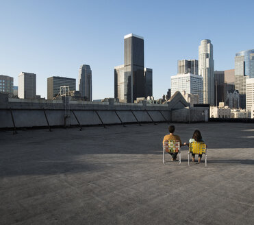 A couple, man and woman sitting in deck chairs on a rooftop overlooking city skyscrapers. - MINF06050