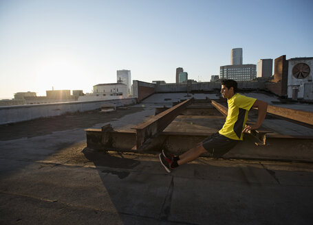 Ein Mann in Sportkleidung auf einem Dach mit Blick auf die Stadt, der Liegestütze auf der Bank macht. - MINF06052