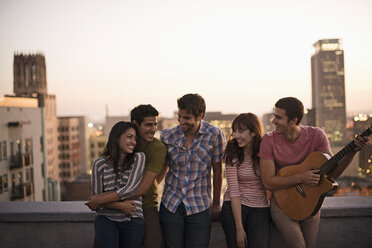 Eine kleine Gruppe von Freunden versammelt sich auf einer Dachterrasse mit Blick auf eine Stadt in der Dämmerung. - MINF06060