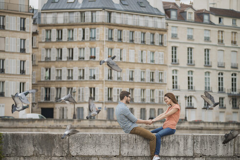 A couple, man and woman sitting on the parapet of a bridge over the River Seine. - MINF06073