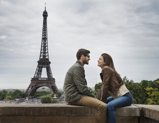 Ein Paar sitzt sich auf einer Mauer in der Stadt Paris gegenüber, mit dem Eiffelturm im Hintergrund. - MINF06074
