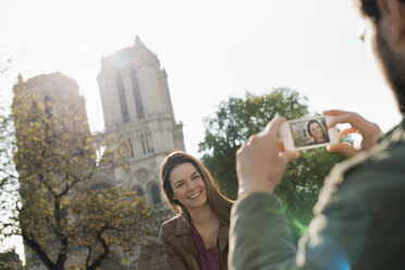 Ein Mann hält ein Smartphone in der Hand und fotografiert eine Frau vor der Kathedrale Notre Dame. - MINF06075