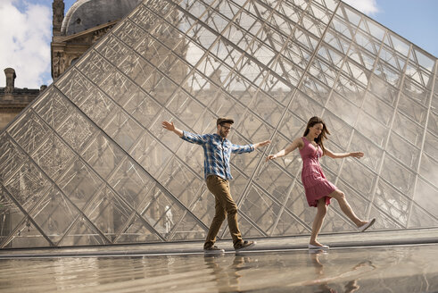 Ein Paar im Innenhof des Louvre-Museums, bei der großen Glaspyramide, mit Springbrunnen und Wasser. - MINF06078