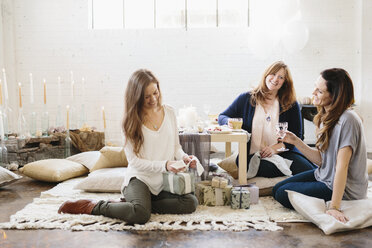 Three women at a celebration, one opening a stack of presents. - MINF06109