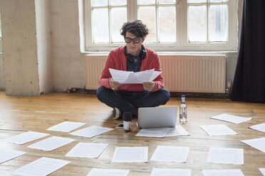 Junger Mann, der in einem Proberaum auf dem Boden sitzt, einen Laptop benutzt und sich Notenblätter ansieht. - MINF06127