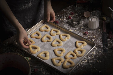 Valentine's Day baking, woman arranging heart shaped biscuits on a baking tray. - MINF06161