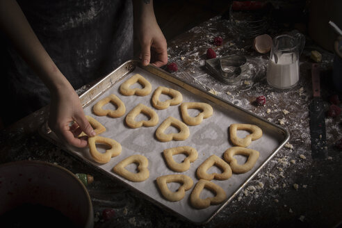 Backen zum Valentinstag, eine Frau legt herzförmige Kekse auf ein Backblech. - MINF06161