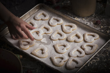 Backen zum Valentinstag, eine Frau legt herzförmige Kekse auf ein Backblech. - MINF06164