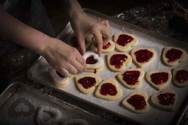 Backen zum Valentinstag, Frau bestreicht herzförmige Kekse mit Himbeermarmelade. - MINF06166