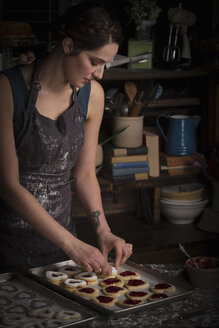 Backen zum Valentinstag, junge Frau steht in einer Küche, mit einem Backblech mit herzförmigen Keksen. - MINF06167